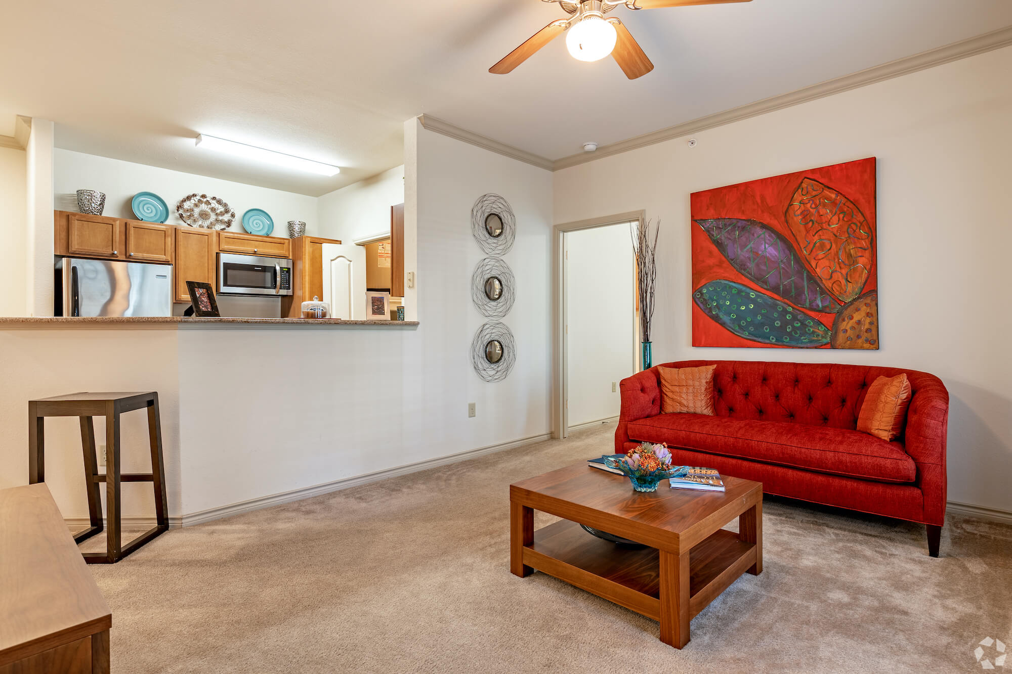 A living room looking into a kitchen with brown cabinets and silver stainless steel appliances.